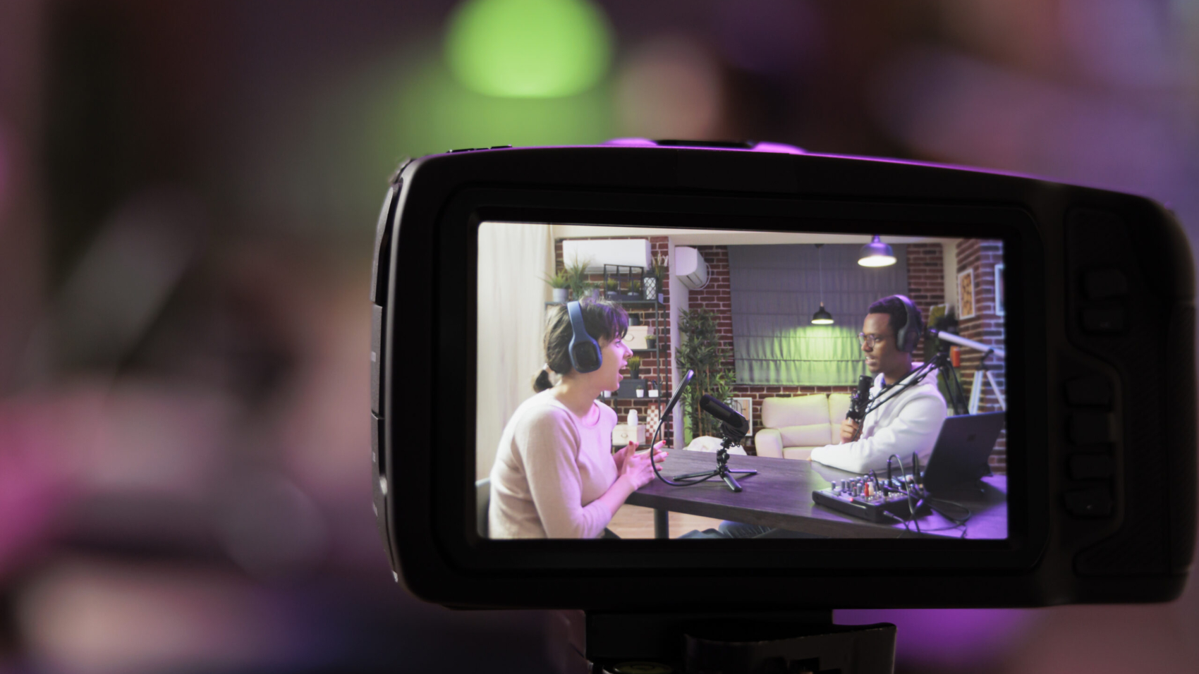 Close up shot focused on preview image on professional camera with podcast host and african american guest enjoying conversation in blurry background. Professional recording equipment in home studio