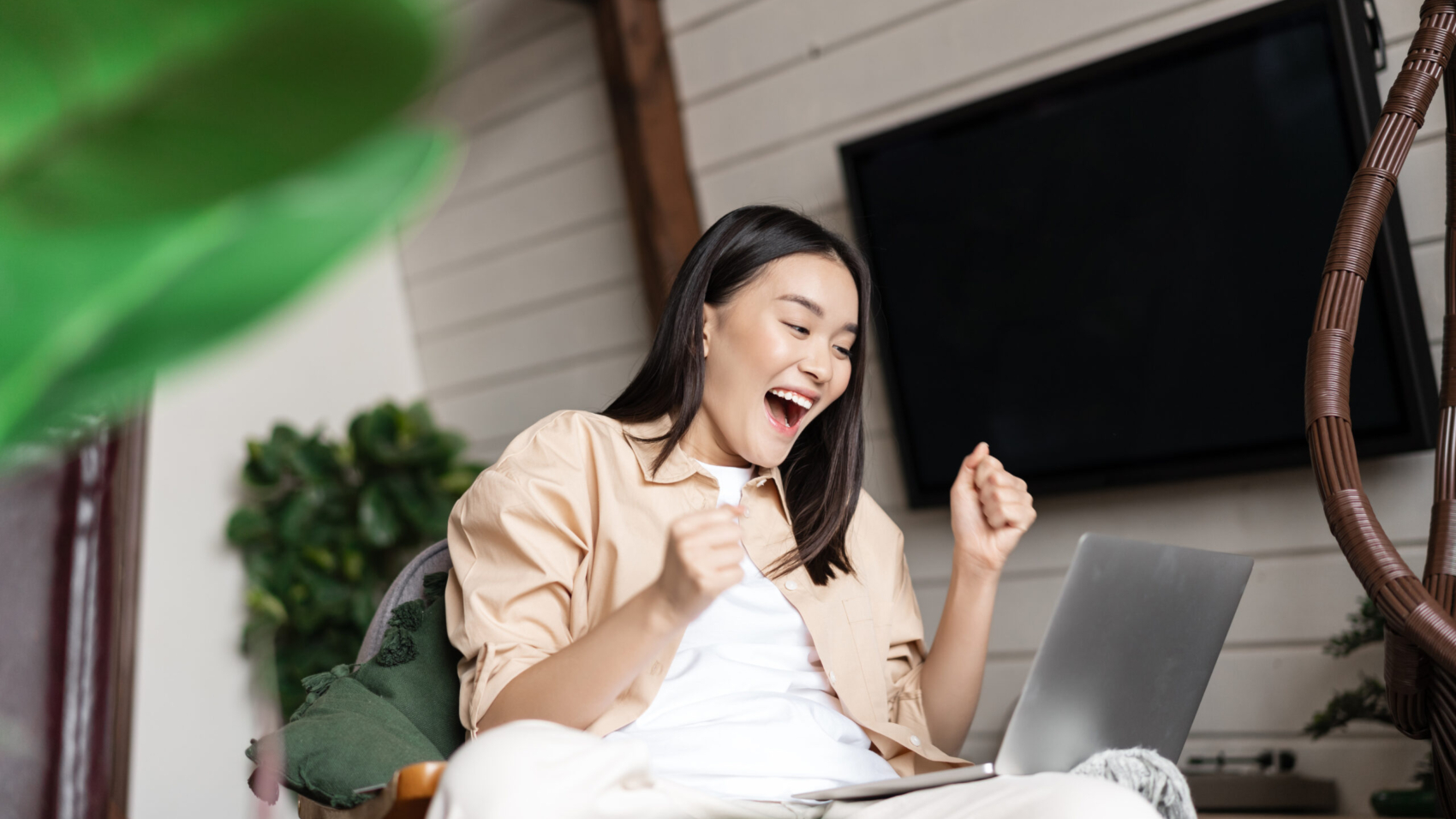 Excited asian girl winning online, rejoicing after looking at laptop screen, sitting at home, cheering and shouting from joy.