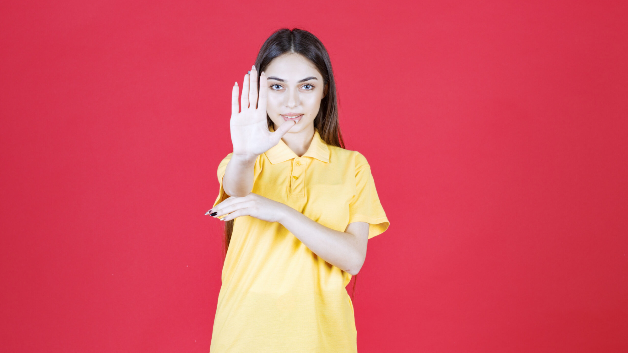 Girl in yellow shirt standing on red background and stopping something. High quality photo